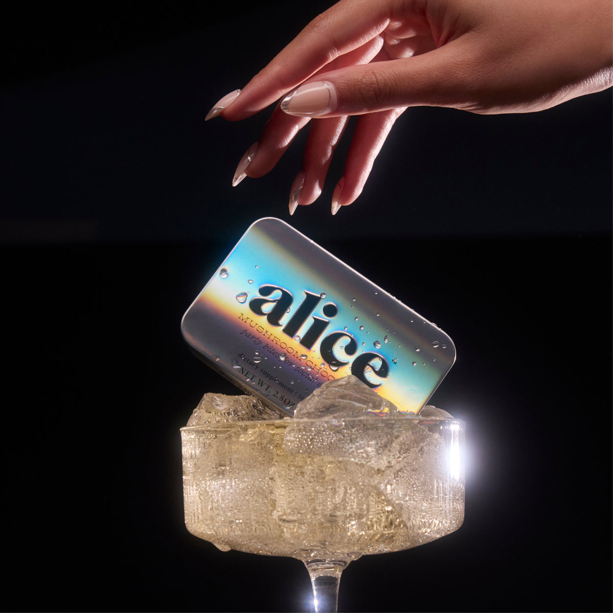Party Trick mushroom chocolate tin, holographic, dropped by hand into a coupe glass of ice against a dark background