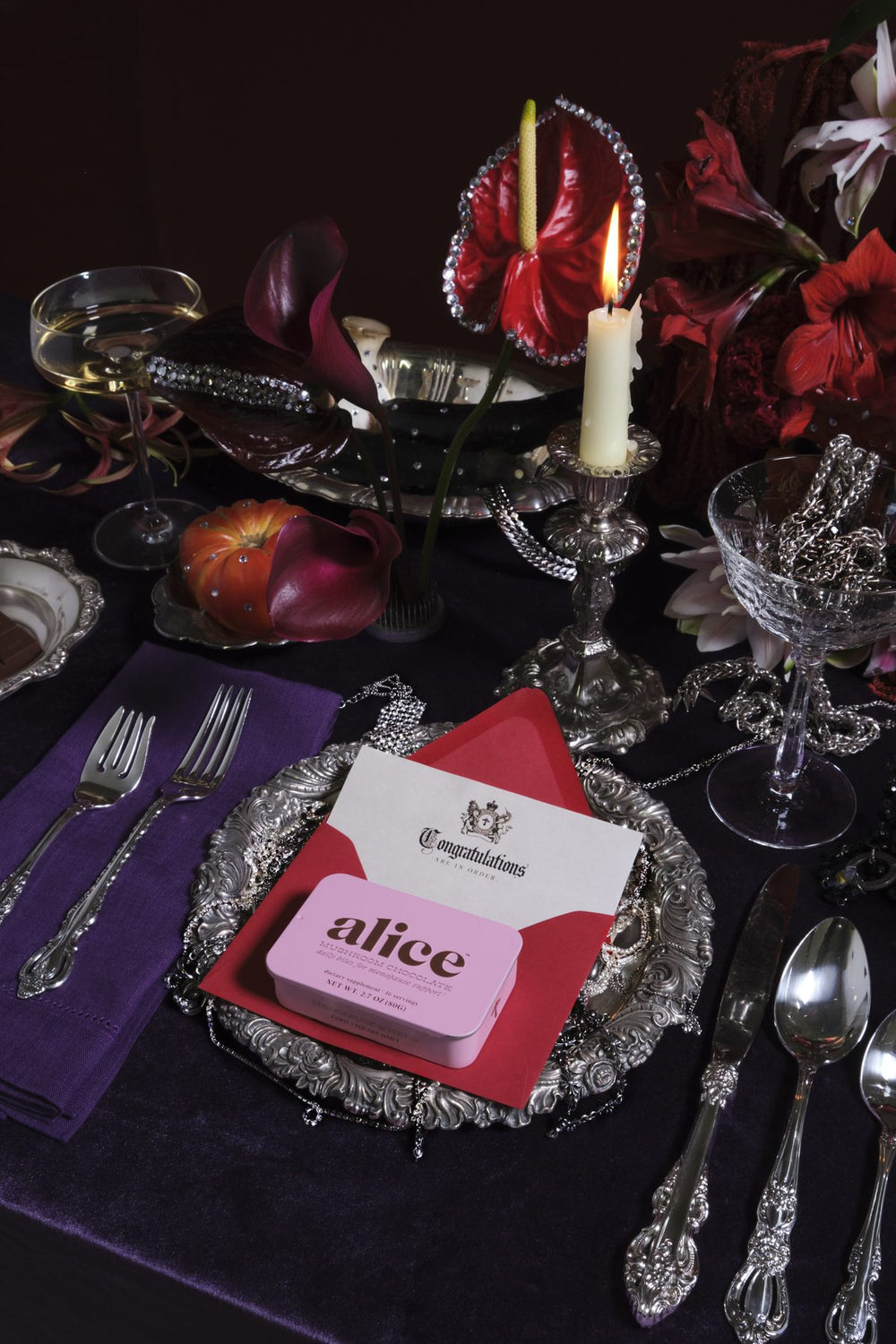 A dinner table set with silver and candles, a Congratulations card and a pink Menopause Hero tin on a red envelope