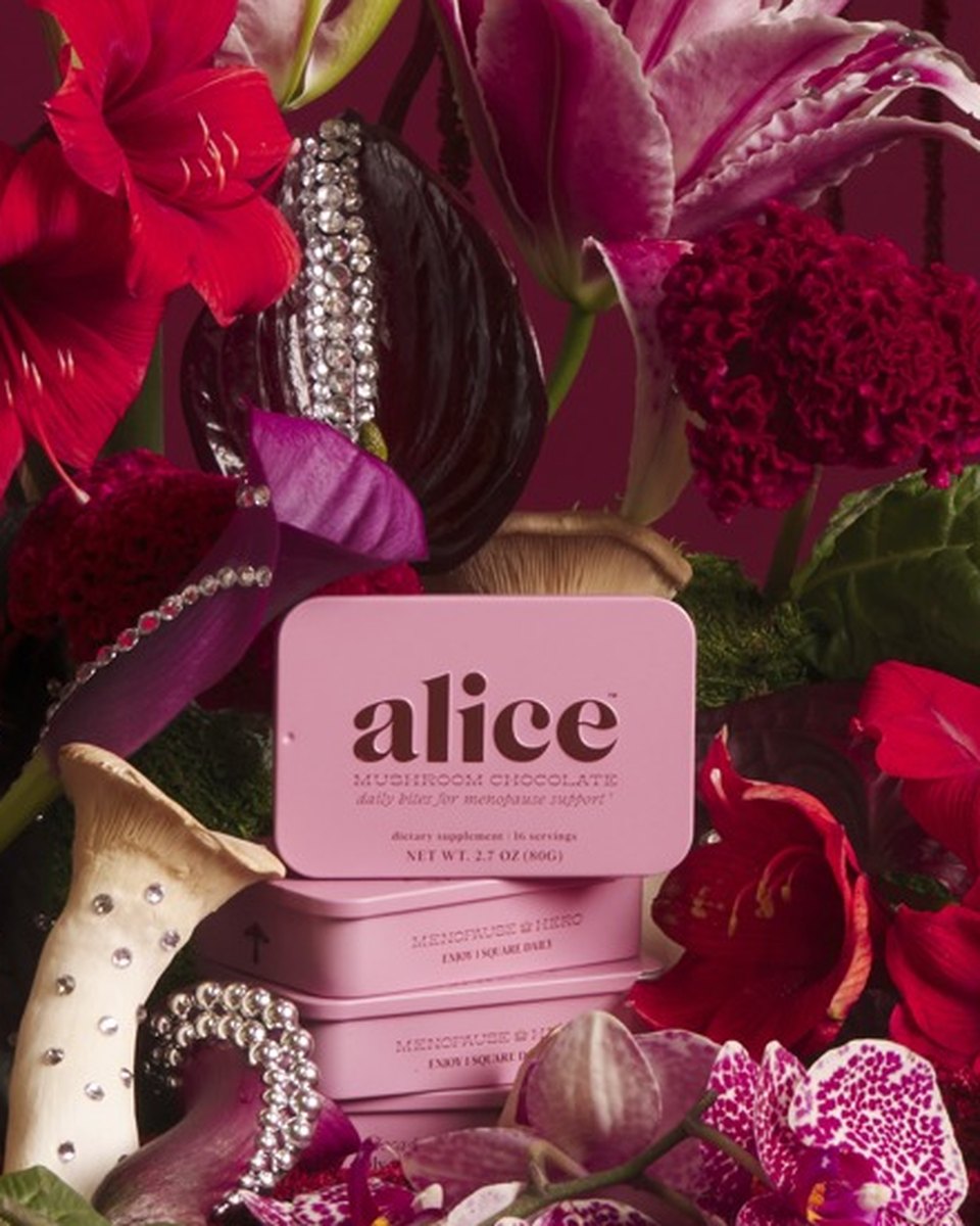 A pink Menopause Hero tin set in a lush arrangement of red anthurium, lilies and florals