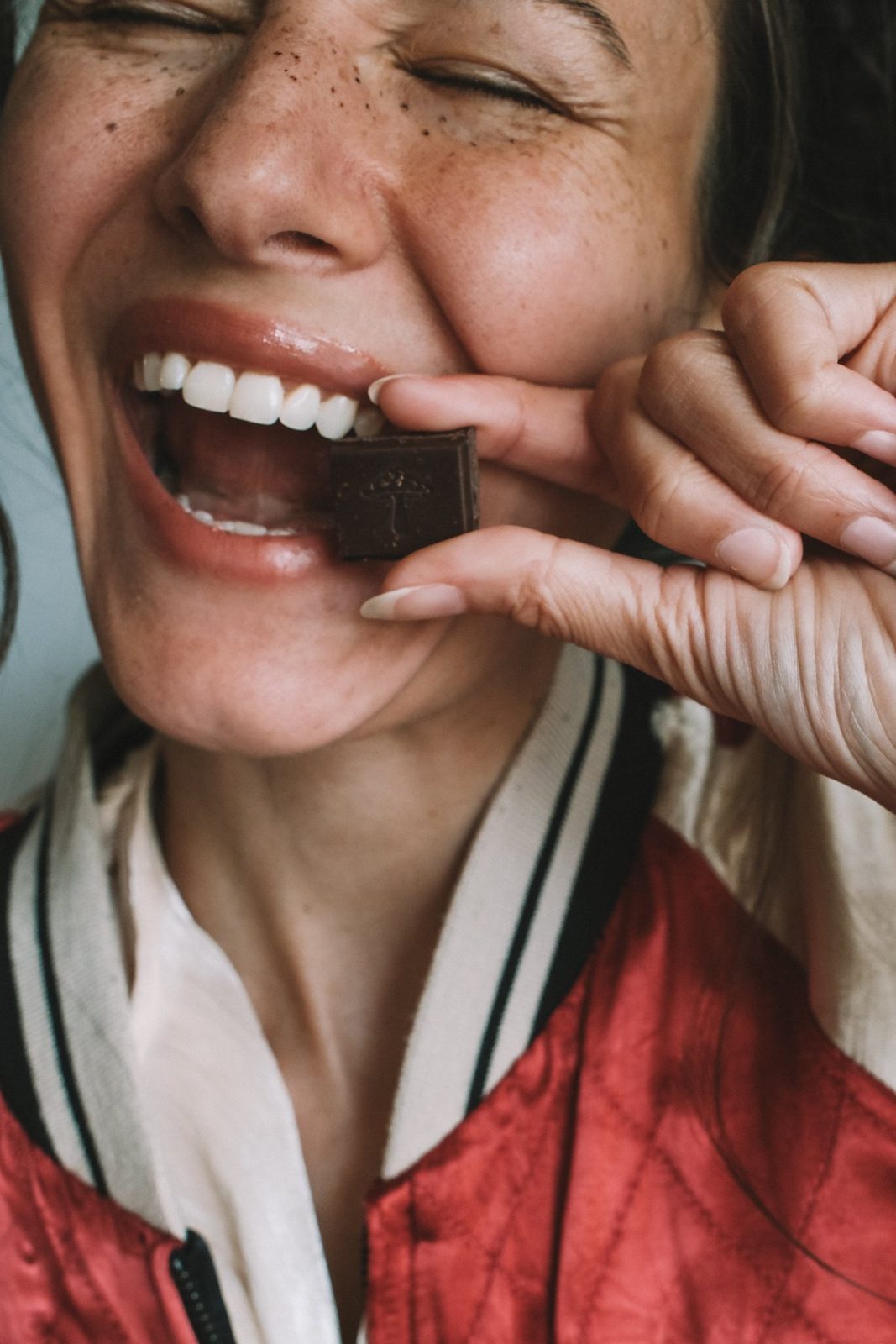 a smiling woman biting a square of alice dark chocolate